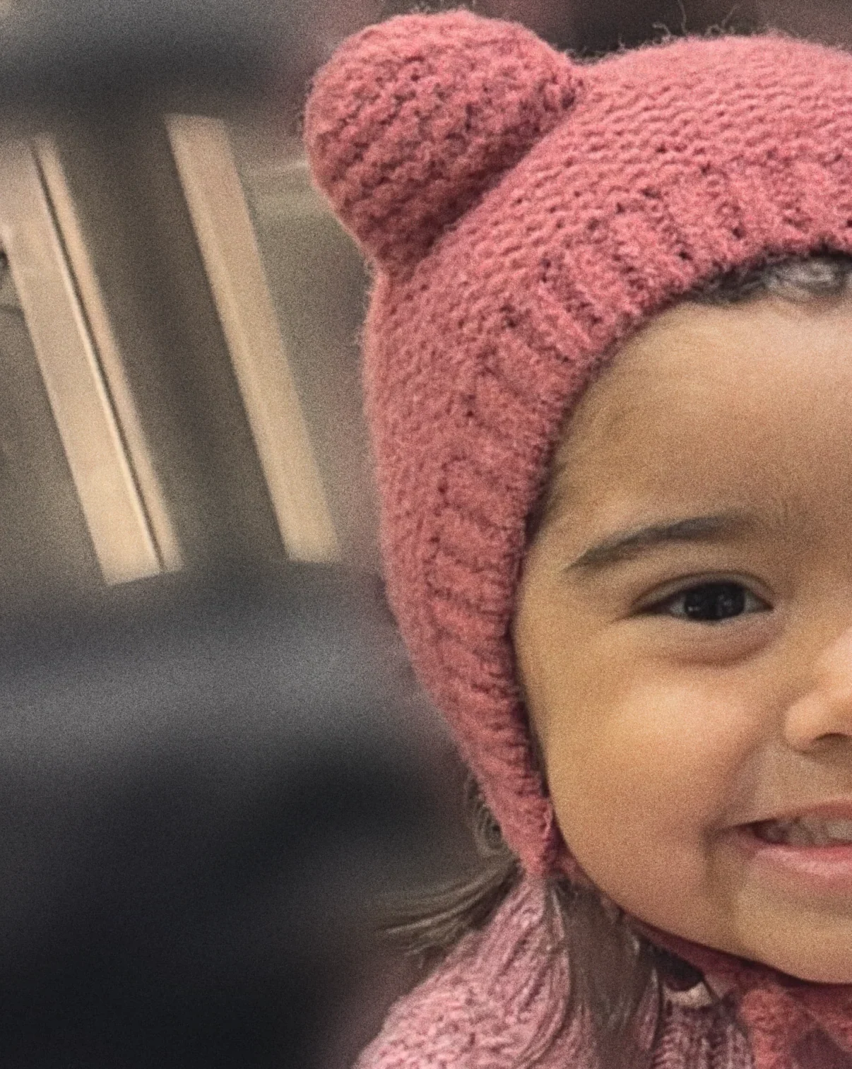 Enfant souriante portant un bonnet en maille framboise à oreilles d’ourson